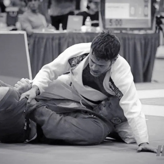 Adult Brazilian Jiu-Jitsu student in a white gi controlling his opponent from top position