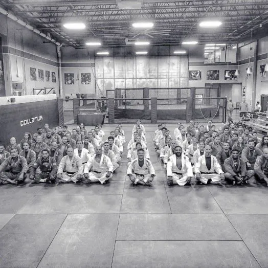 Rows of American Top Team jiu-jitsu students and black belts in white gis seated on the mats